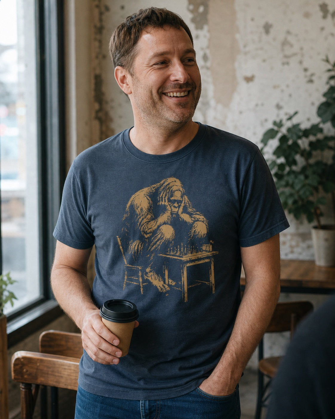 A man wearing the Big Think chess tee shares a coffee and a laugh in a café